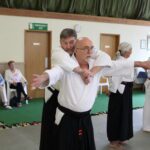 One student, held in a bear hug, draws his arms out and forwards to bring his partner's balance forward.